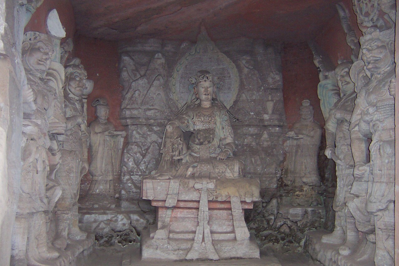 Seated Guanyin figure with halo and attendant figures within a Beishan niche