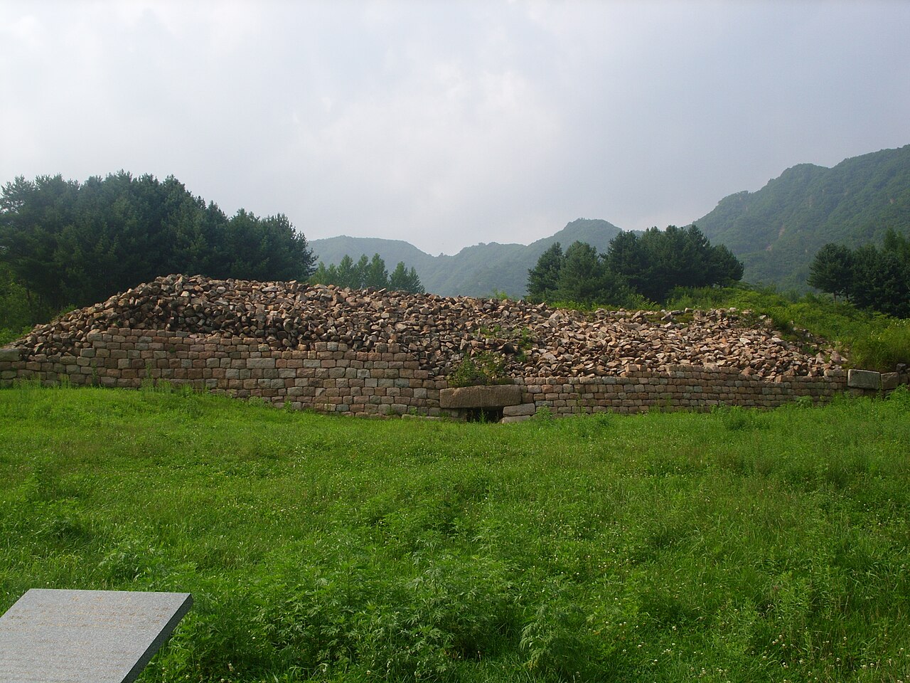 Low stone remains at Wandu Mountain City with wooded hills beyond