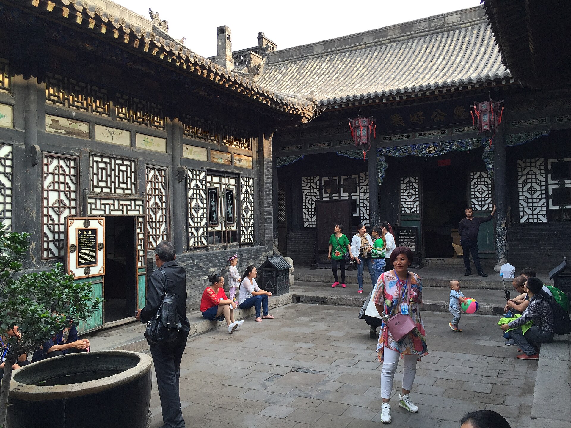 Visitors in a Rishengchang courtyard surrounded by tiled roofs, doors and labelled rooms